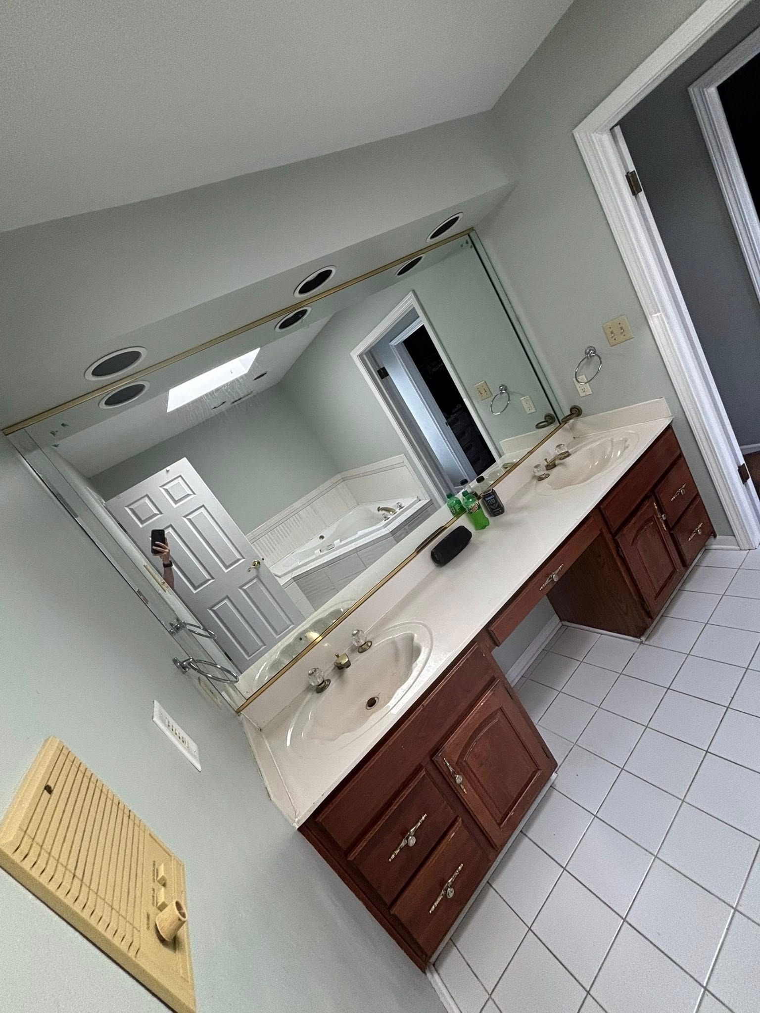 Bathroom with double sinks, brown cabinets, white countertop, large mirror, and white tiled floor.