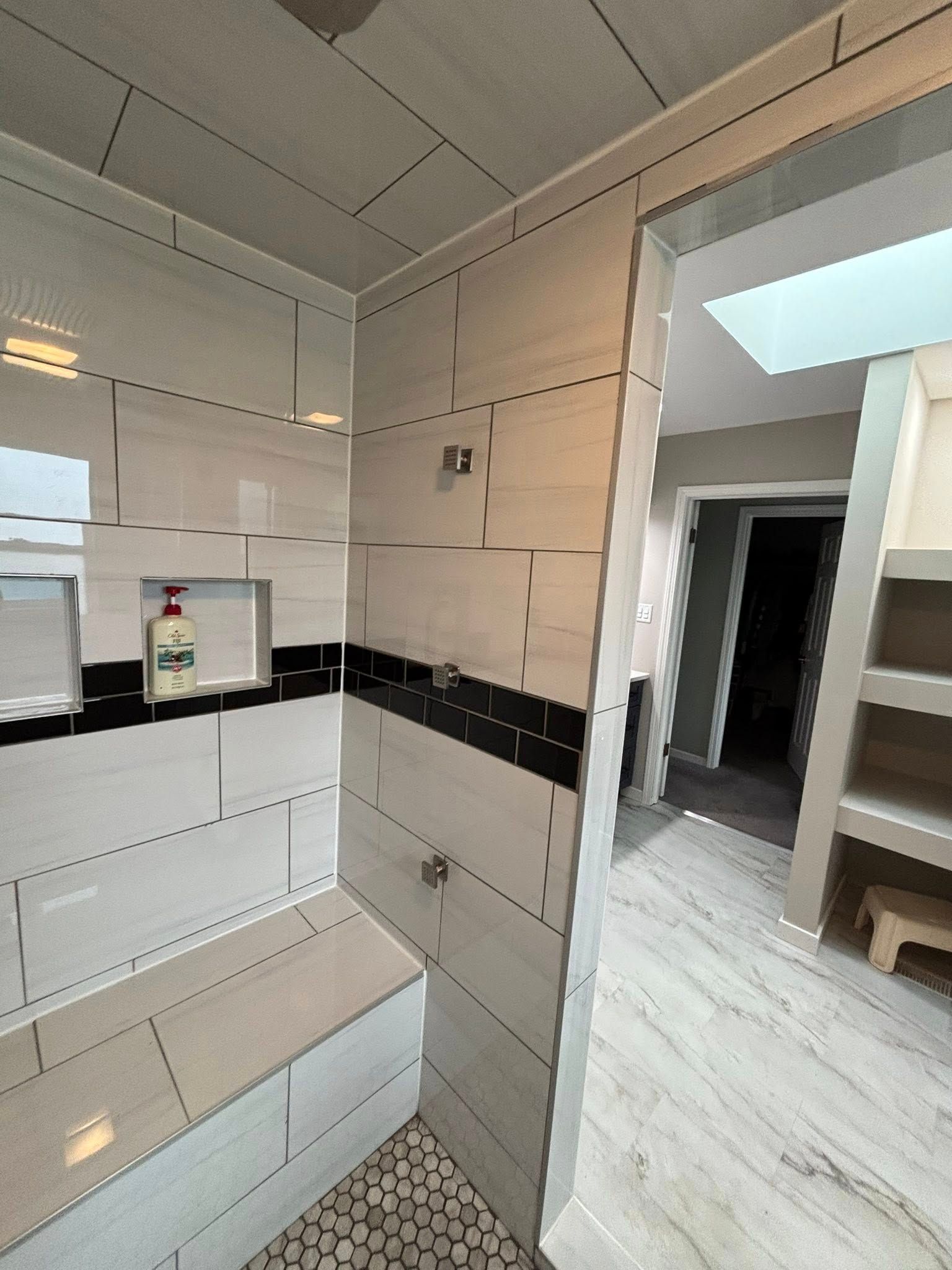 Bathroom with light gray tile walls, a black tile stripe, and a pebble floor in the shower area.