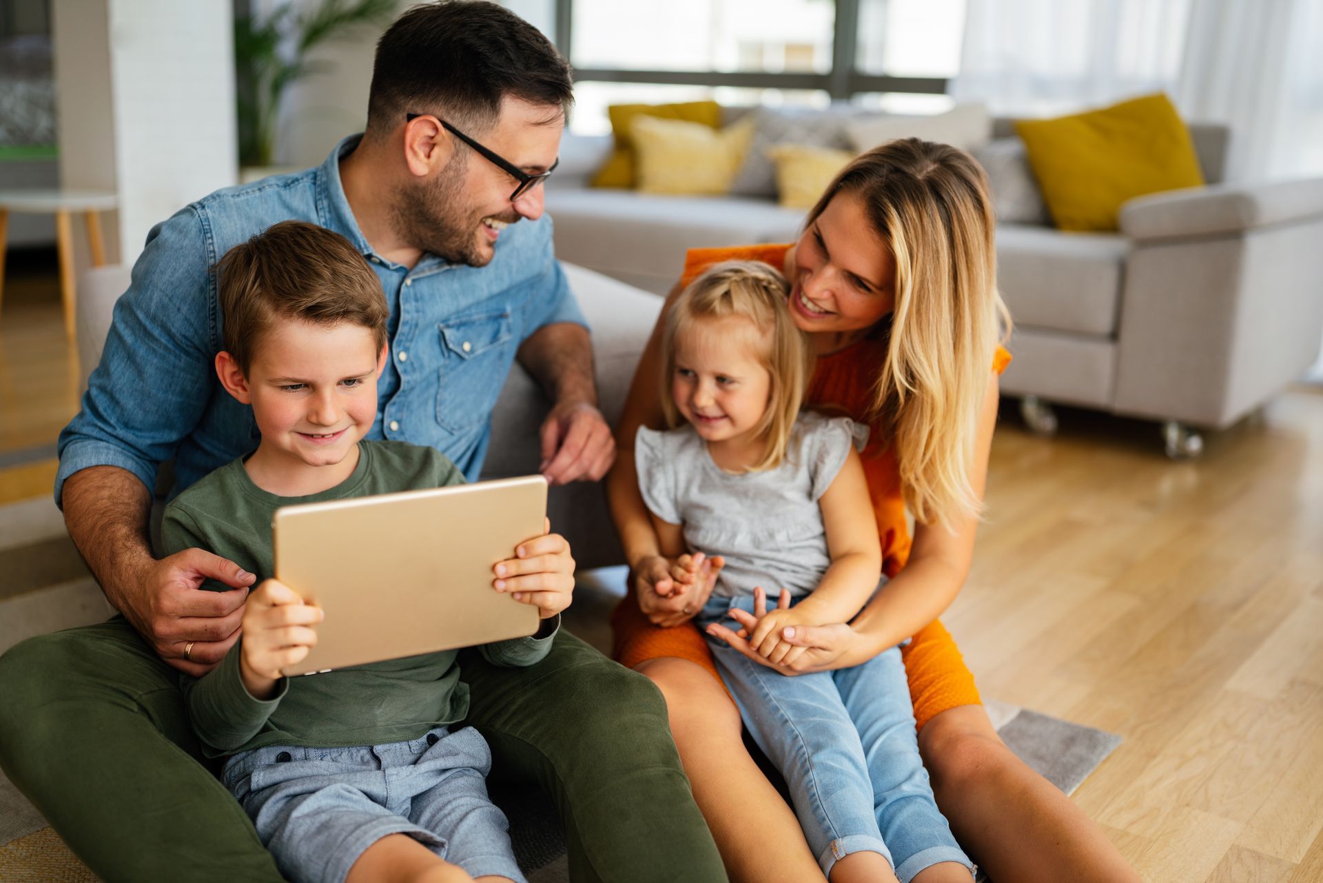A family is sitting on the floor looking at a tablet.