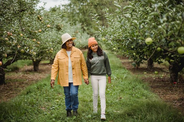 Two women are walking through an apple orchard holding hands.