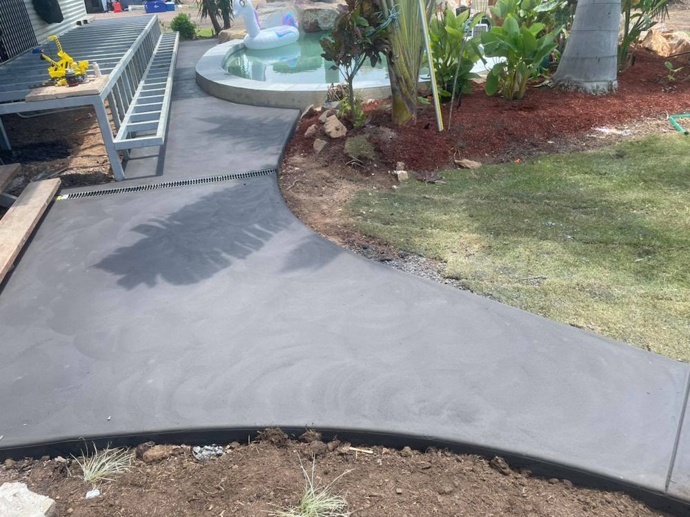 Newly Poured Dark Gray Concrete Walkway Curves by a Pool and Grass Lawn — Mobcon Construction in Berry Springs, NT