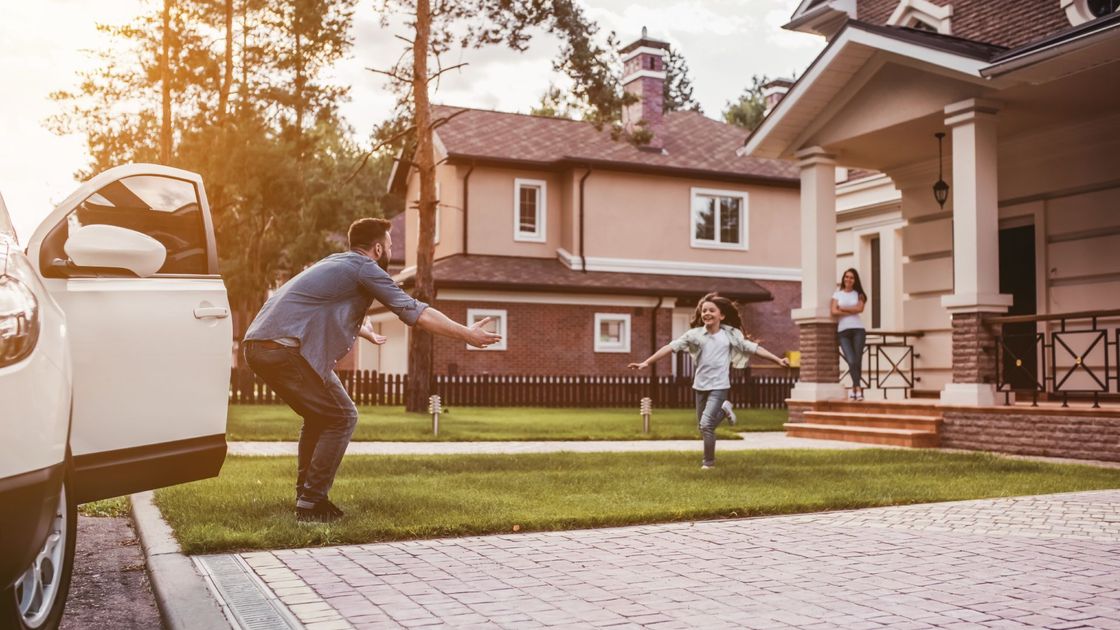 A man is helping a child get out of a car in front of a house.