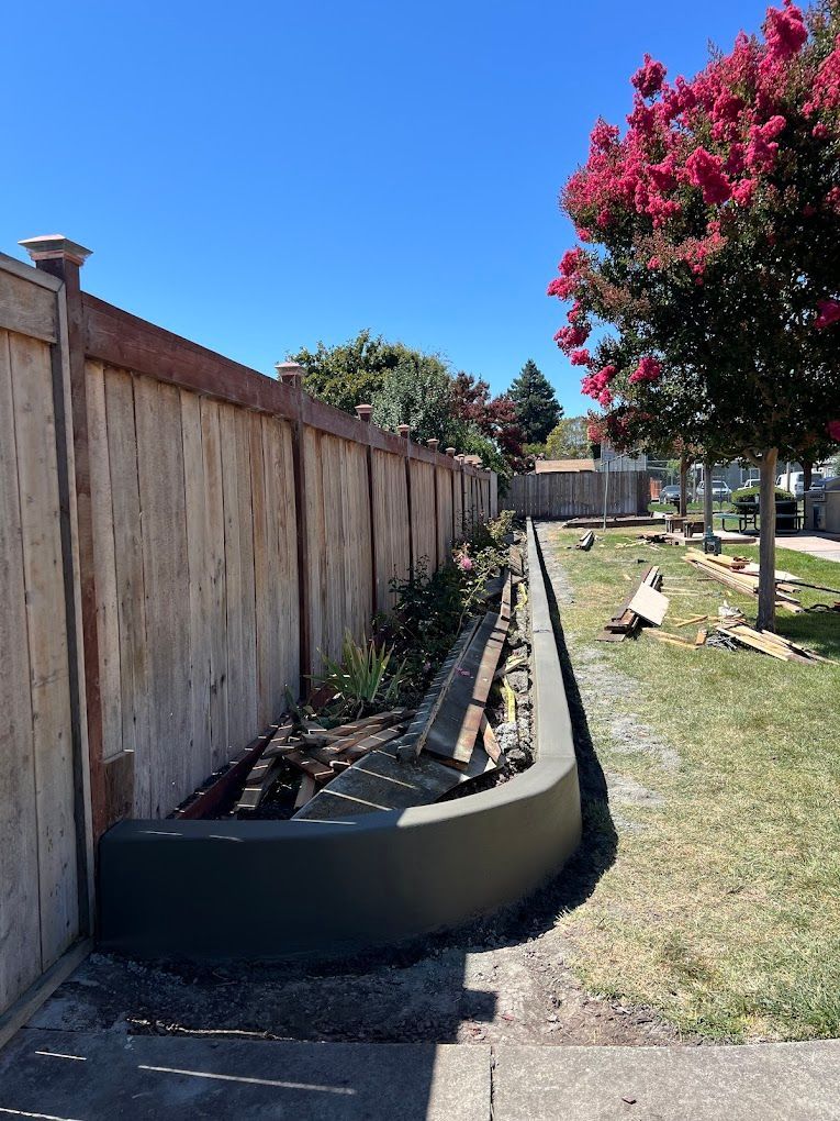 A wooden fence surrounds a lush green yard with a tree in the background.