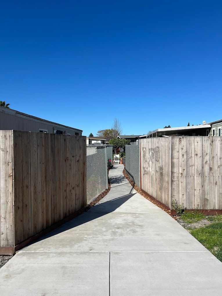 A concrete walkway between two wooden fences on a sunny day