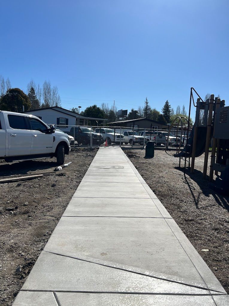 A white truck is parked on the side of a concrete walkway leading to a playground.
