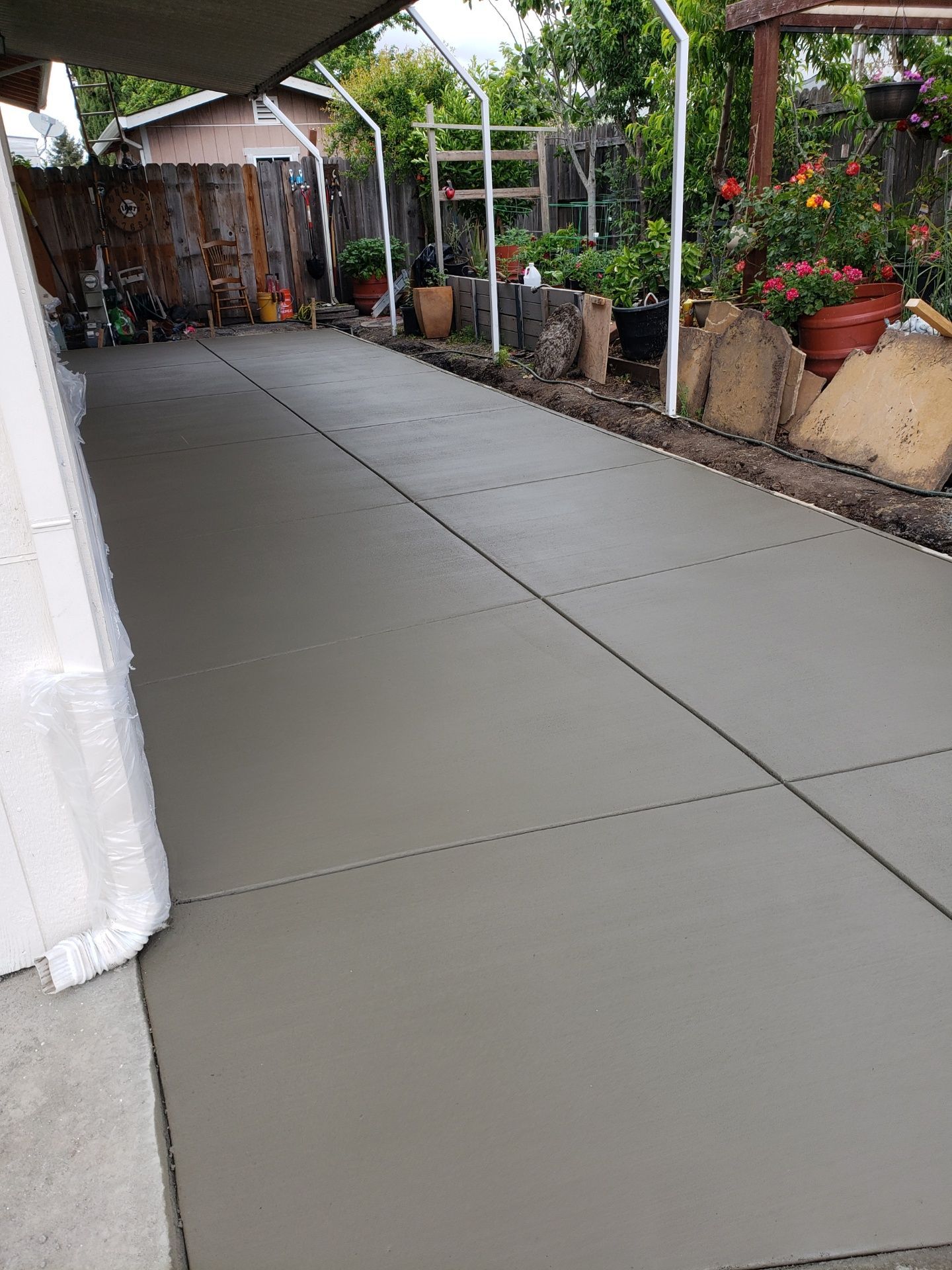 A concrete driveway leading to a backyard filled with potted plants.