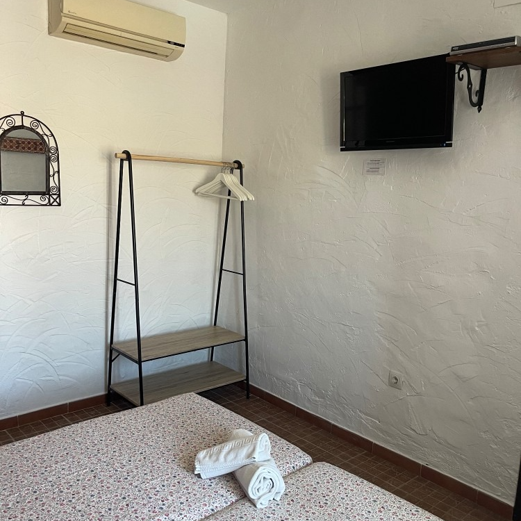 A bedroom with a bed , clothes rack , television and mirror.