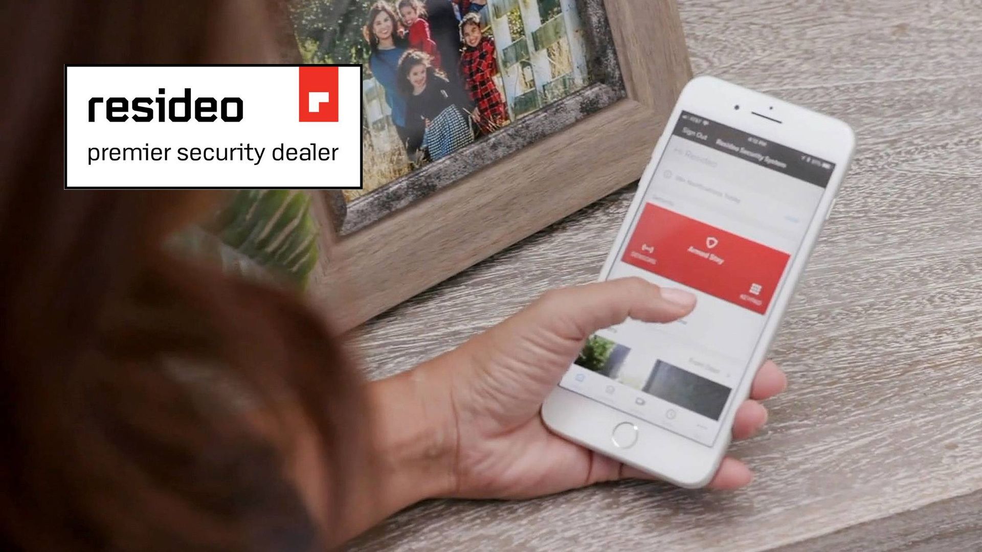 Woman using a smartphone with security app, framed photo in background, Resideo logo at left.
