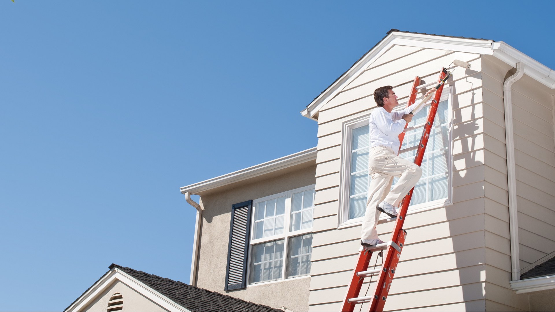 Man on ladder painting siding of a house, sunny day.