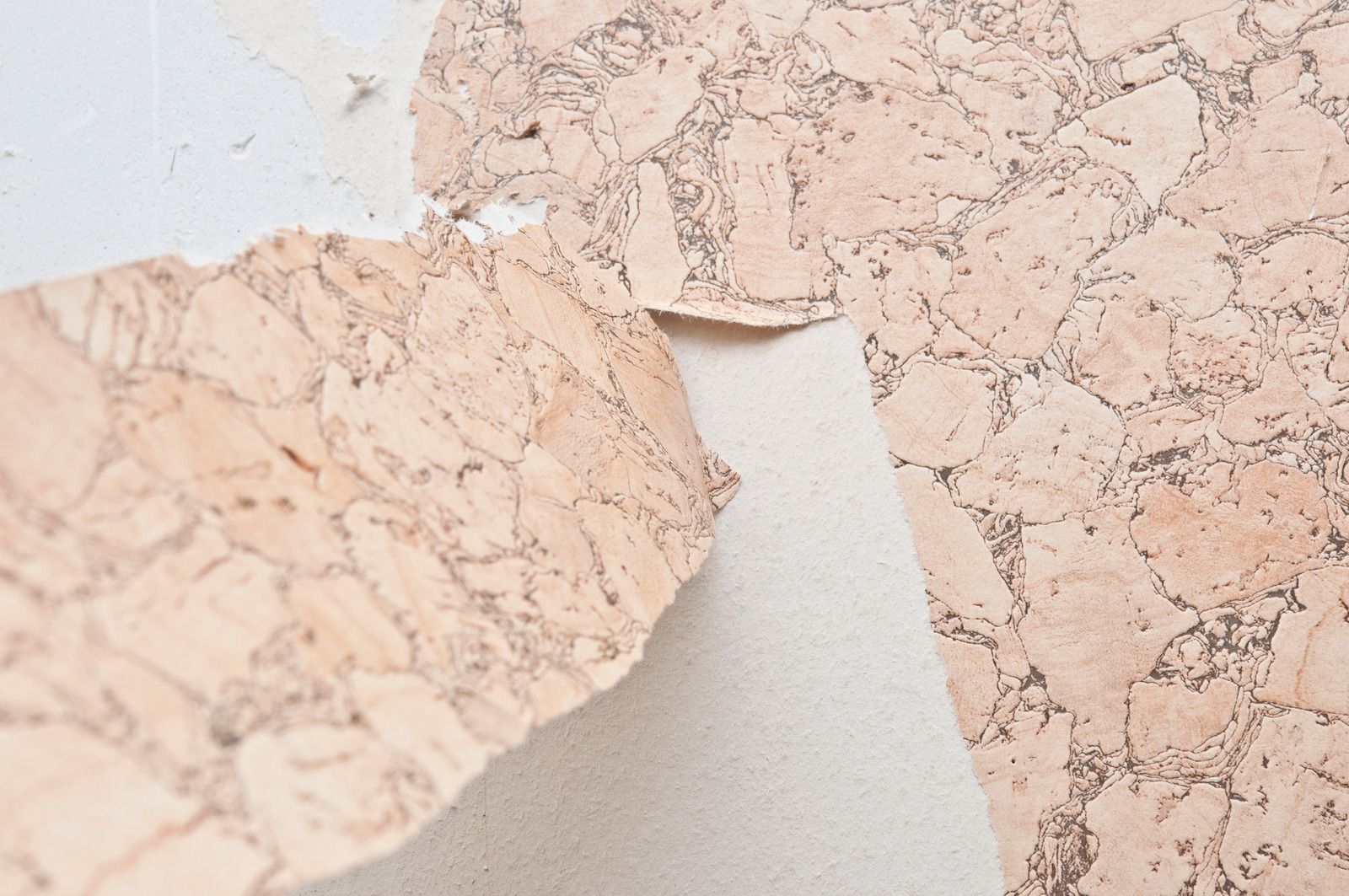 Cork wallpaper partially peeled off a white wall.