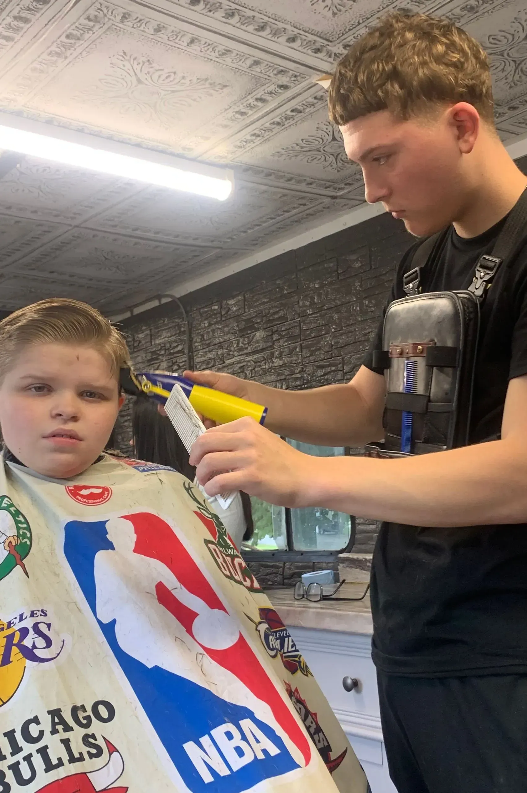 A young boy is getting his hair cut by a barber wearing a chicago bulls cape.