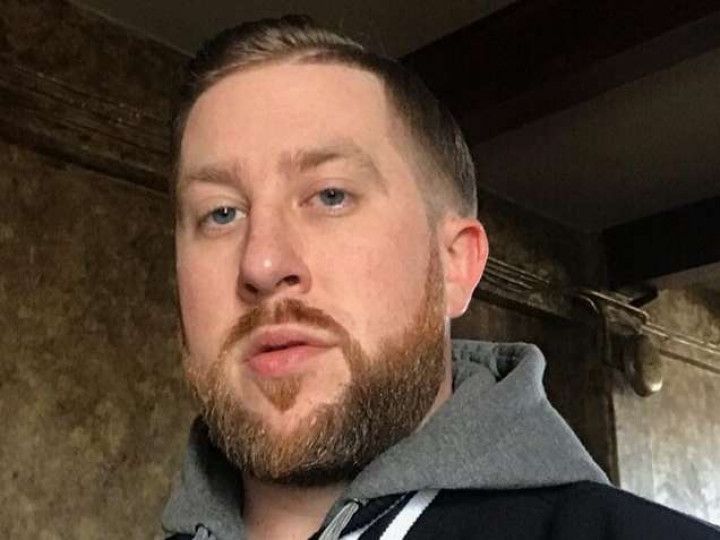 A man with a beard is wearing a hoodie and looking at the camera.
