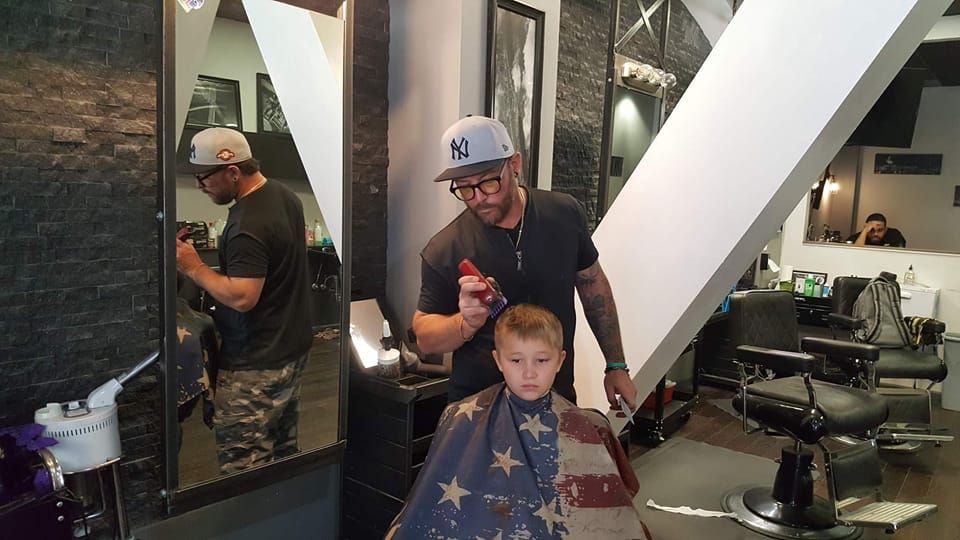A young boy is getting his hair cut by a barber in a barber shop.