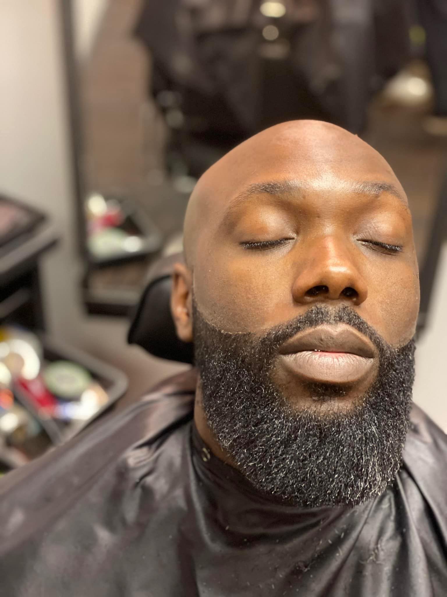 A bald man with a beard is sitting in a chair with his eyes closed.