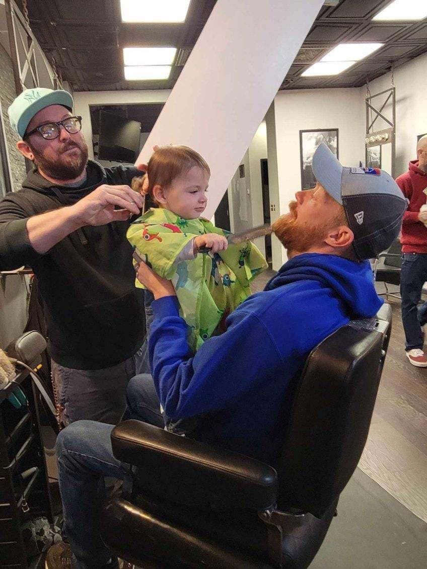 A man is cutting a baby 's hair in a barber shop.