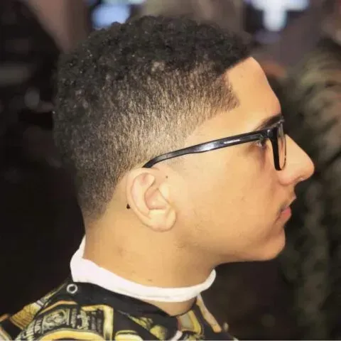 A young man wearing glasses and a choker is getting his hair cut by a barber.