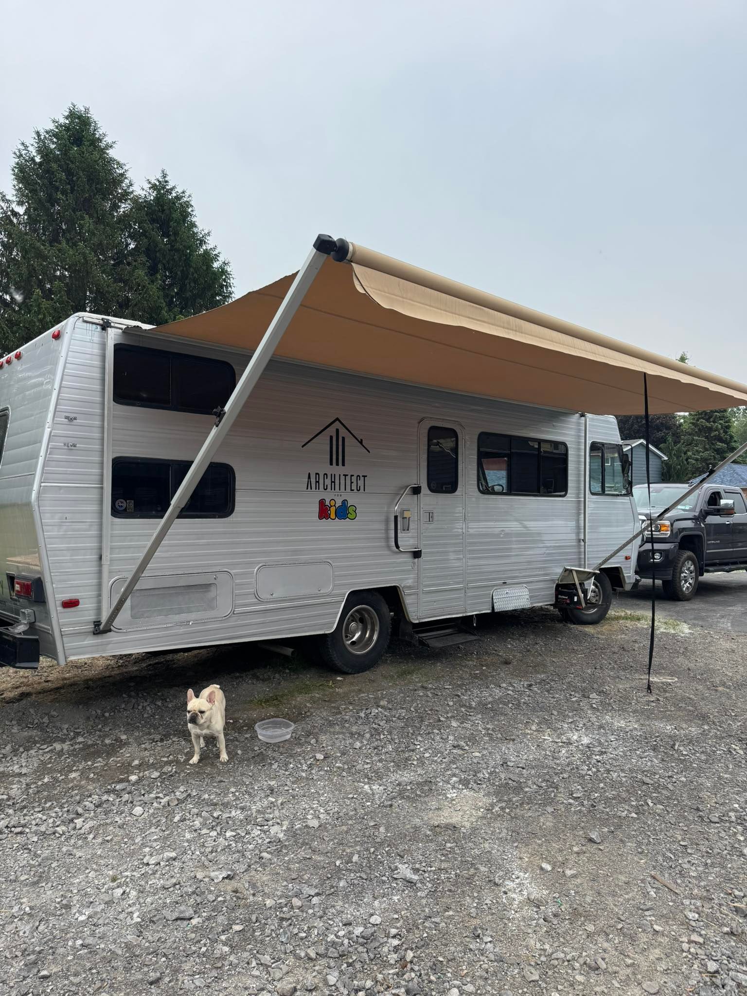 A white rv with an awning is parked in a gravel lot.
