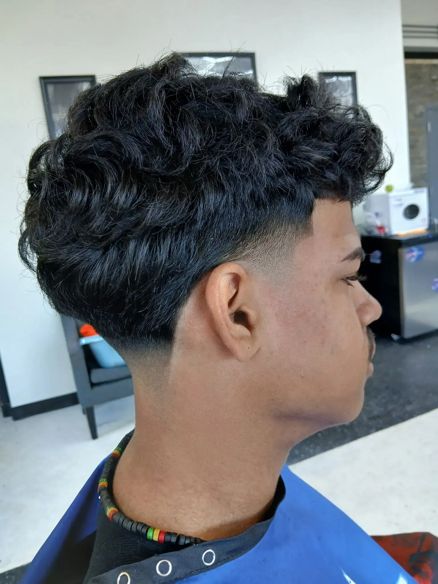 A young man with curly hair is getting his hair cut at a barber shop.