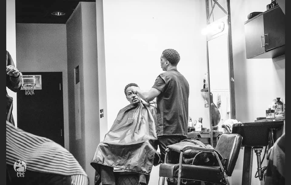 A man is getting his hair cut by a barber in a black and white photo.