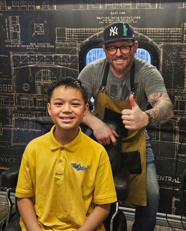 A man wearing a ny hat giving a thumbs up next to a young boy