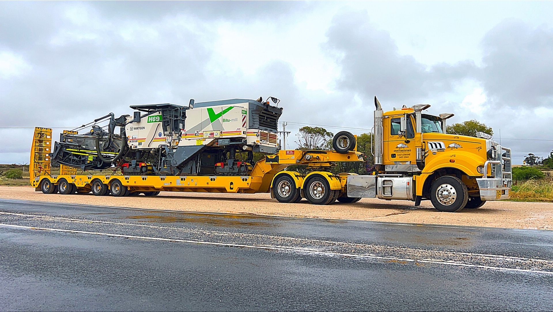 A yellow semi truck is carrying a large machine on a trailer.