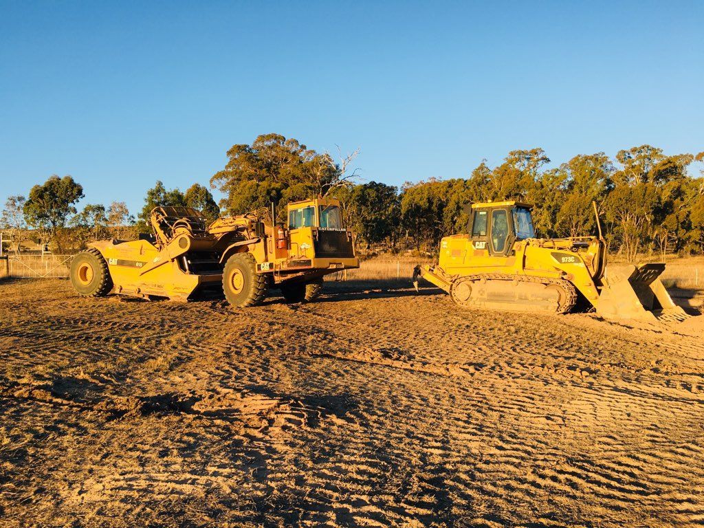 Two yellow excavators in a dirt field.