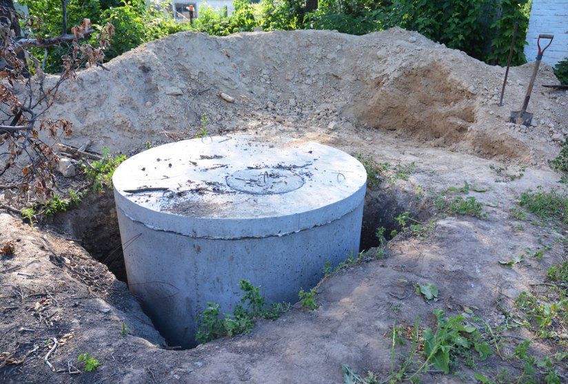 Concrete septic tank lids installed on a sloped, freshly excavated hillside, with surrounding greenery and service vehicles in the background — TCP Plumbing in Tenterfield, NSW