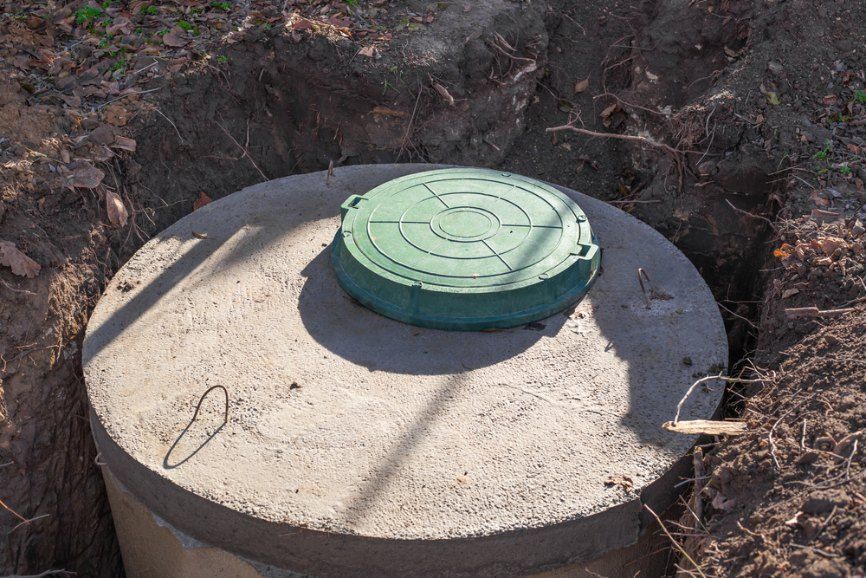 A Concrete Septic Tank With a Green Lid is Sitting in the Dirt — TCP Plumbing in Bonalbo, NSW