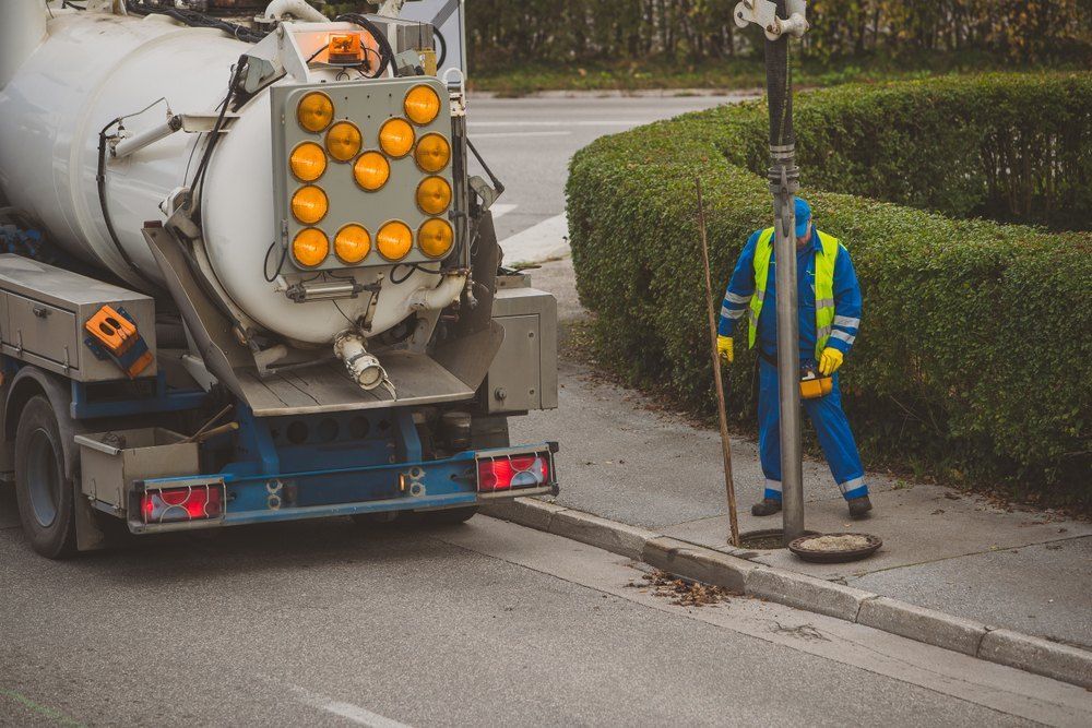 A Man is Cleaning a Manhole Cover Next to a Vacuum Truck — TCP Plumbing in Casino, NSW
