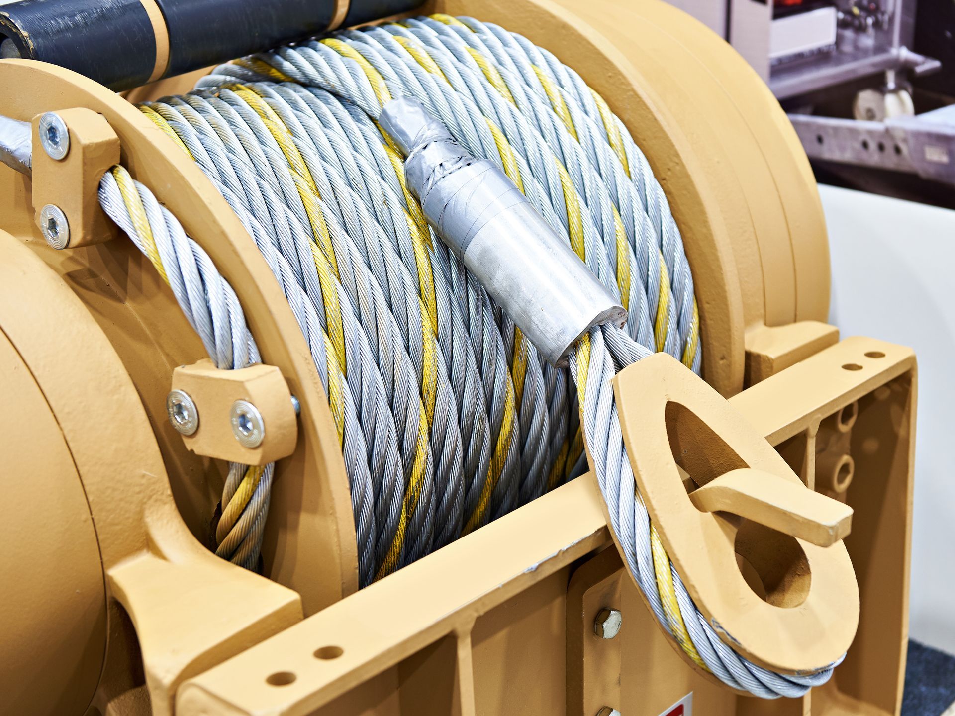Yellow winch with coiled steel cable. Close-up view of the hardware with hook attachment.