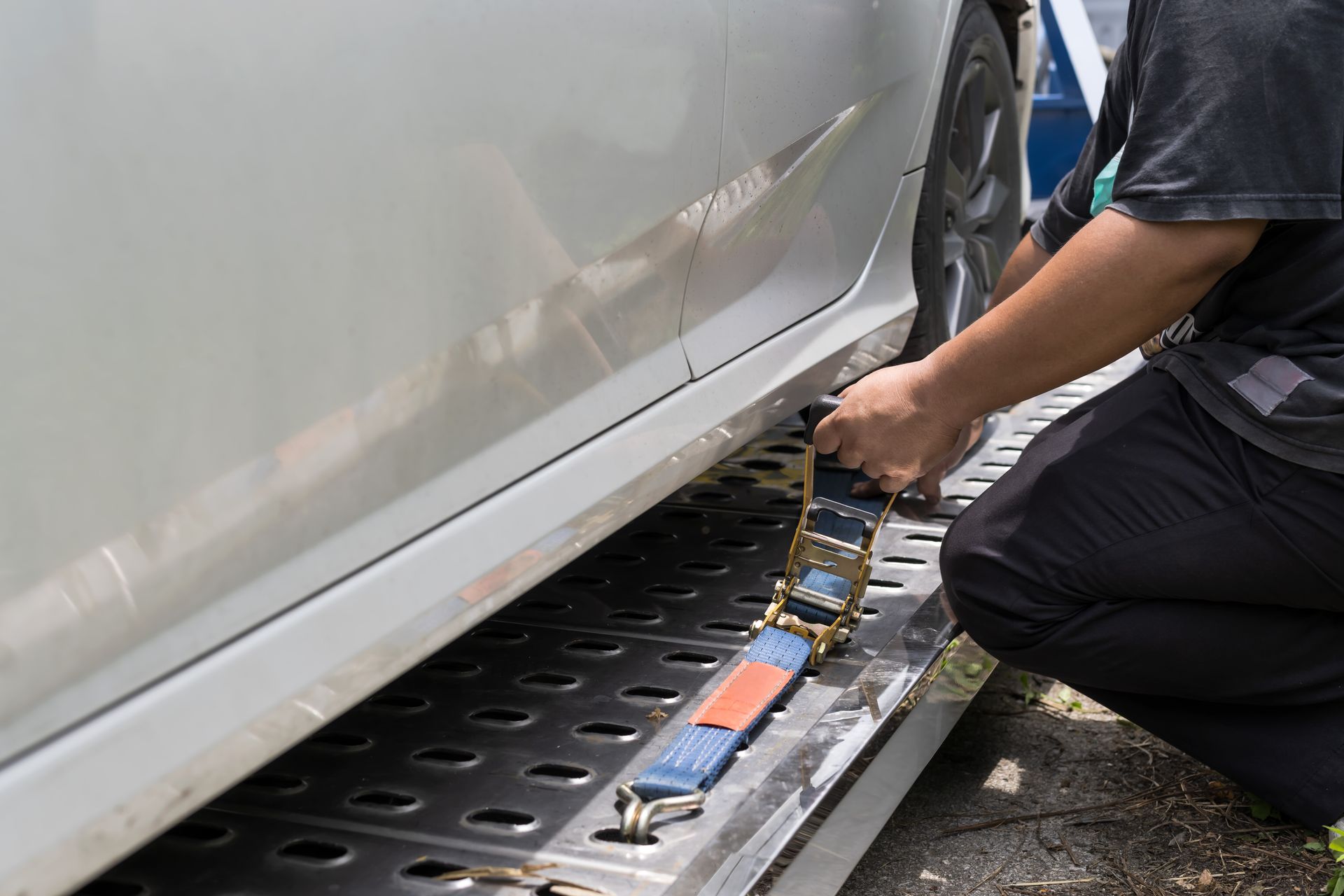 Person secures a car to a tow truck bed with a strap.