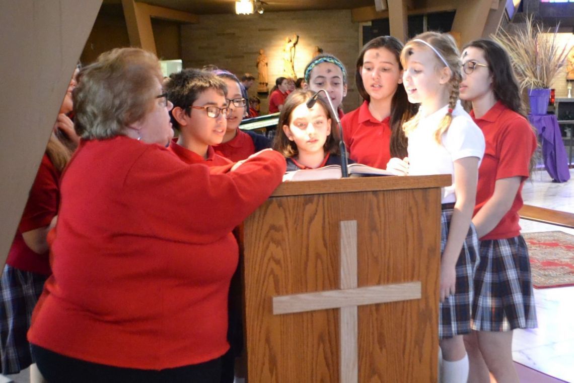 A group of children are standing around a wooden podium with a cross on it
