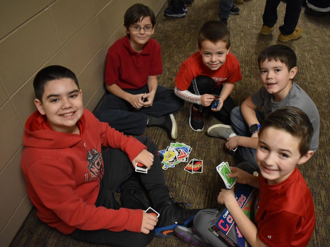 A group of young boys are sitting on the floor playing uno
