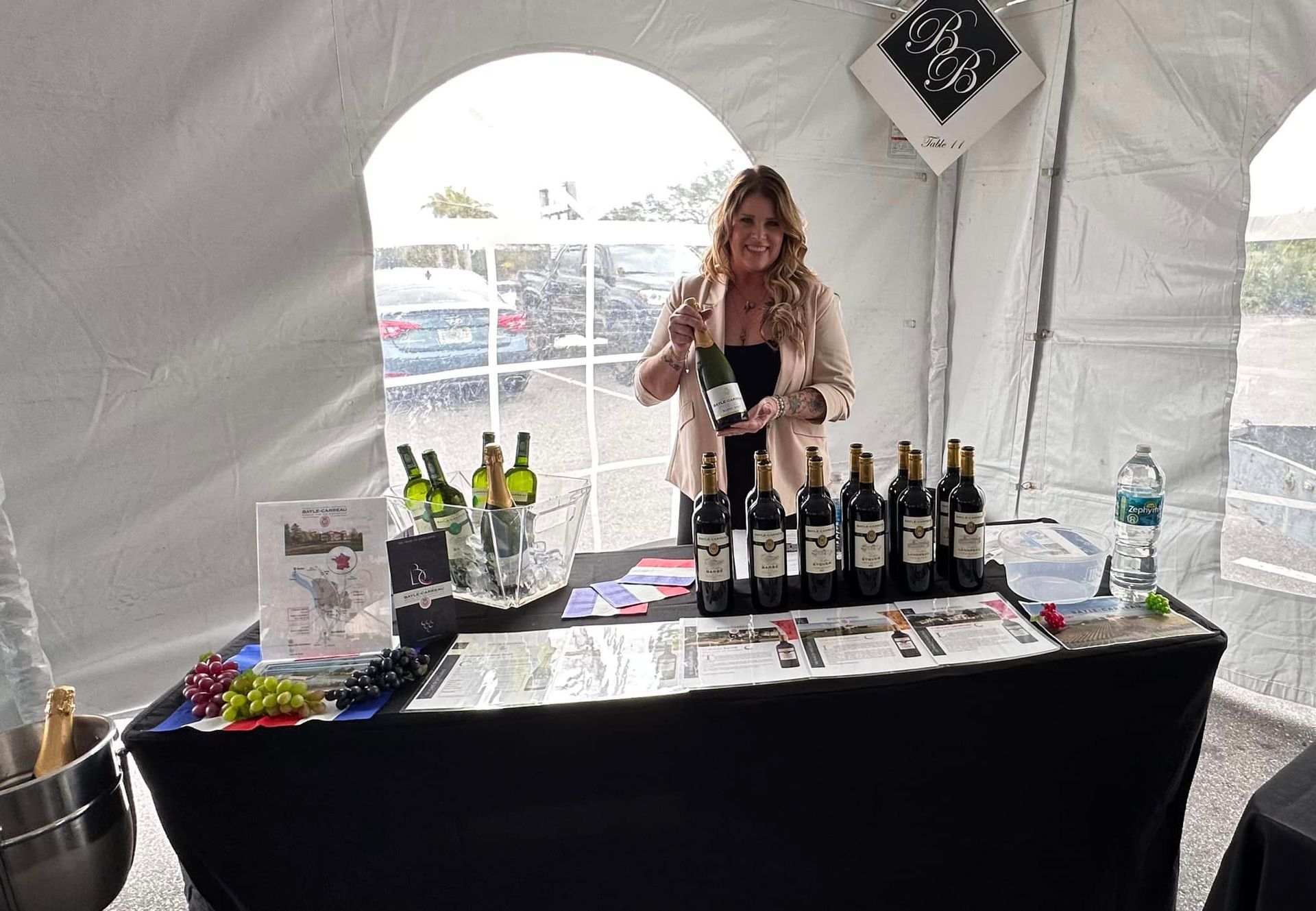 A woman is standing behind a table with bottles of wine on it.