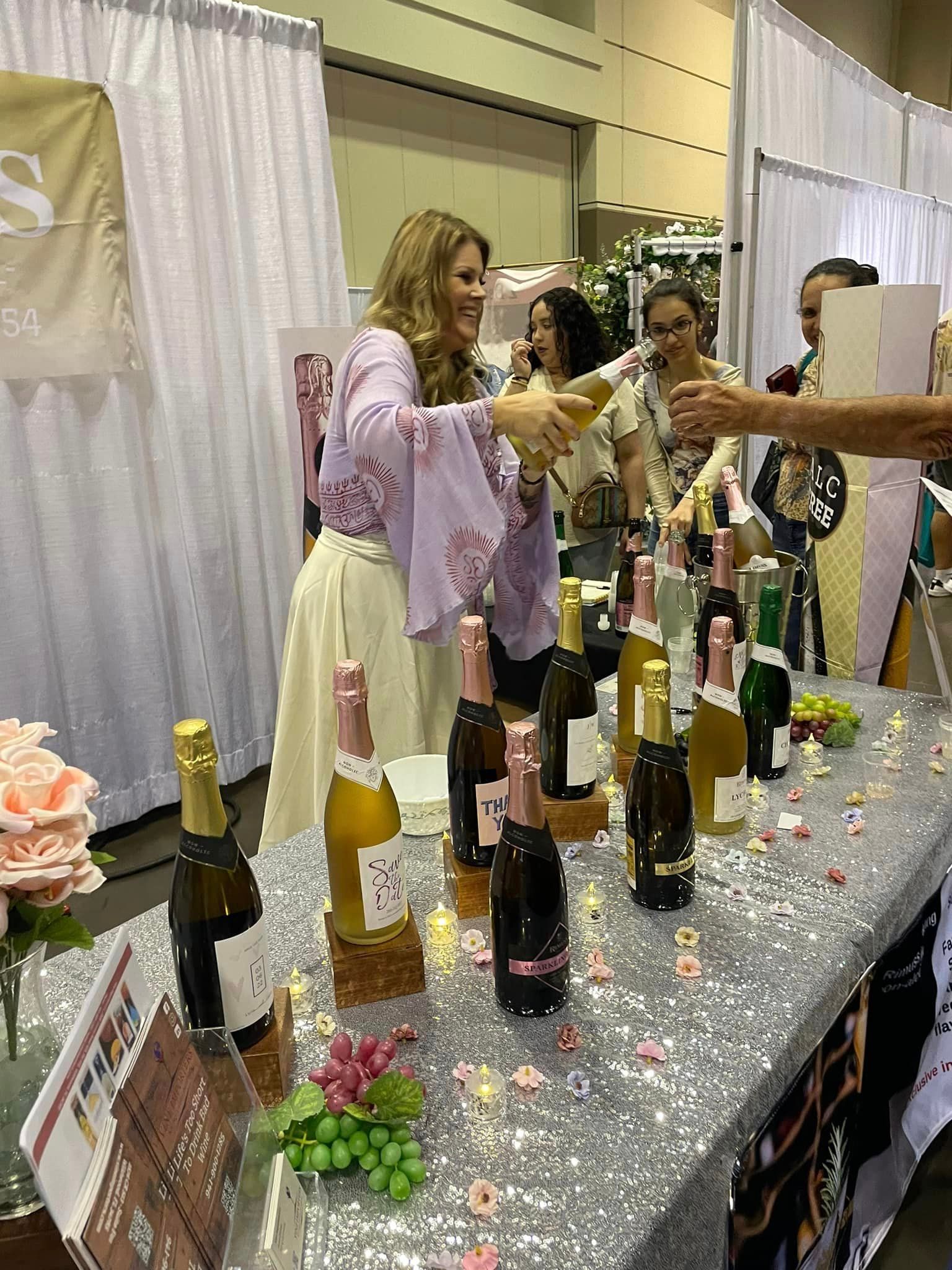 A group of people are standing around a table filled with bottles of wine.