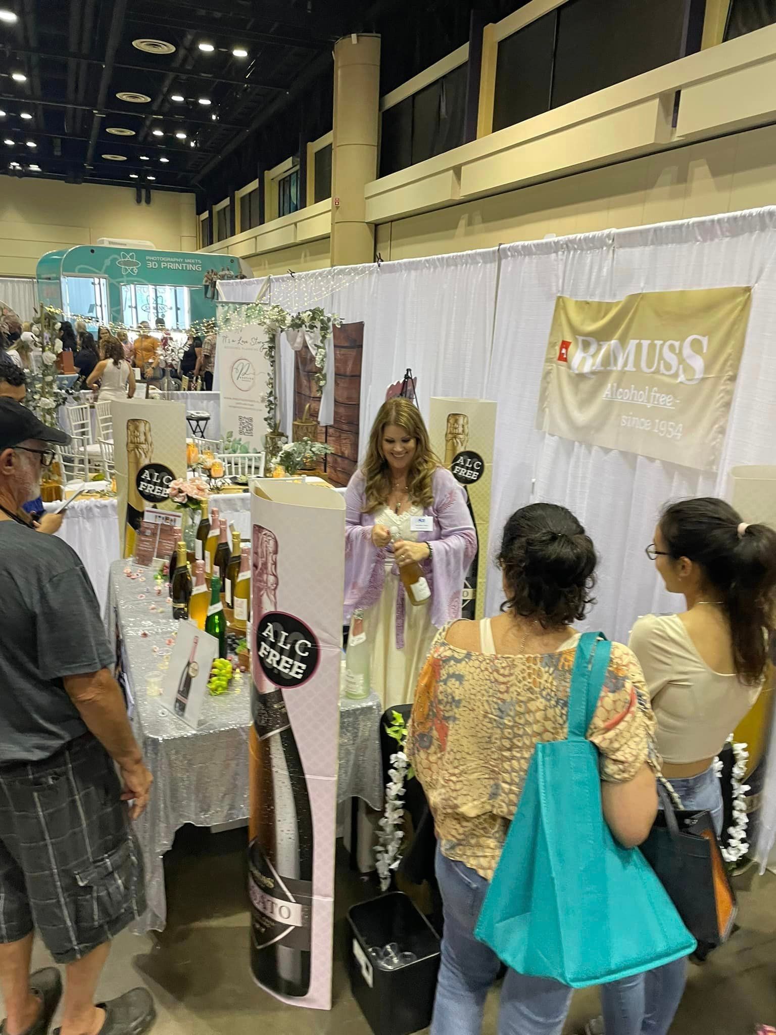 A woman in a purple dress is standing in front of a table with bottles of wine.