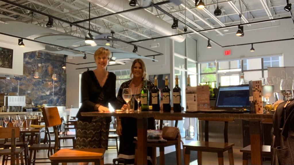 Two women are sitting at a table with bottles of wine.