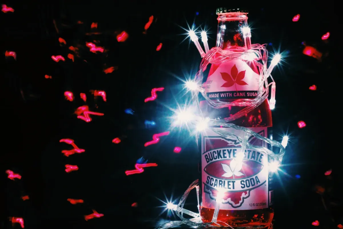 A bottle of honeydew flavored soda is surrounded by lights and confetti.