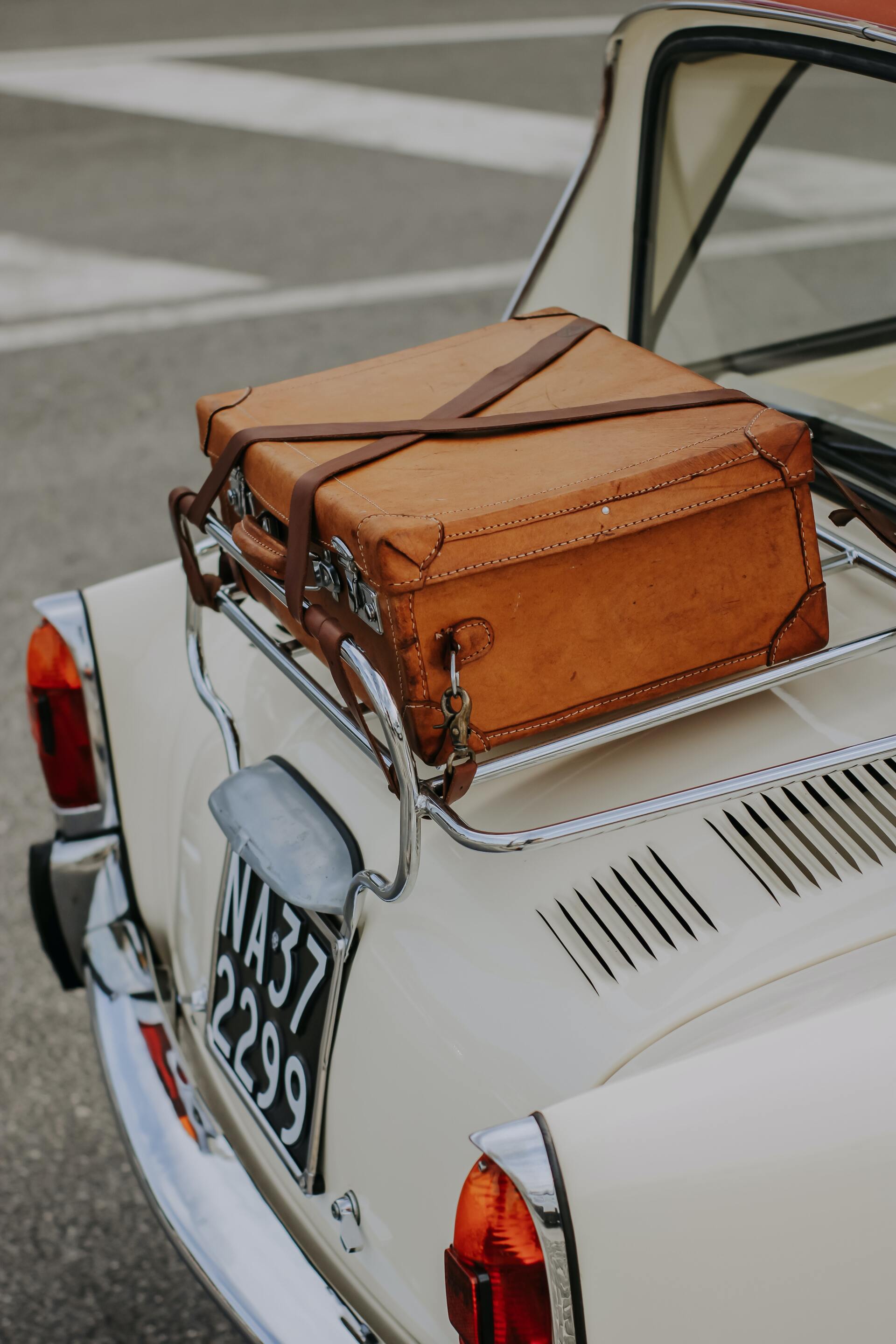 A white car with a brown suitcase on the back rack.