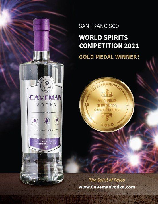 A bottle of caveman vodka is sitting on a table with fireworks in the background.
