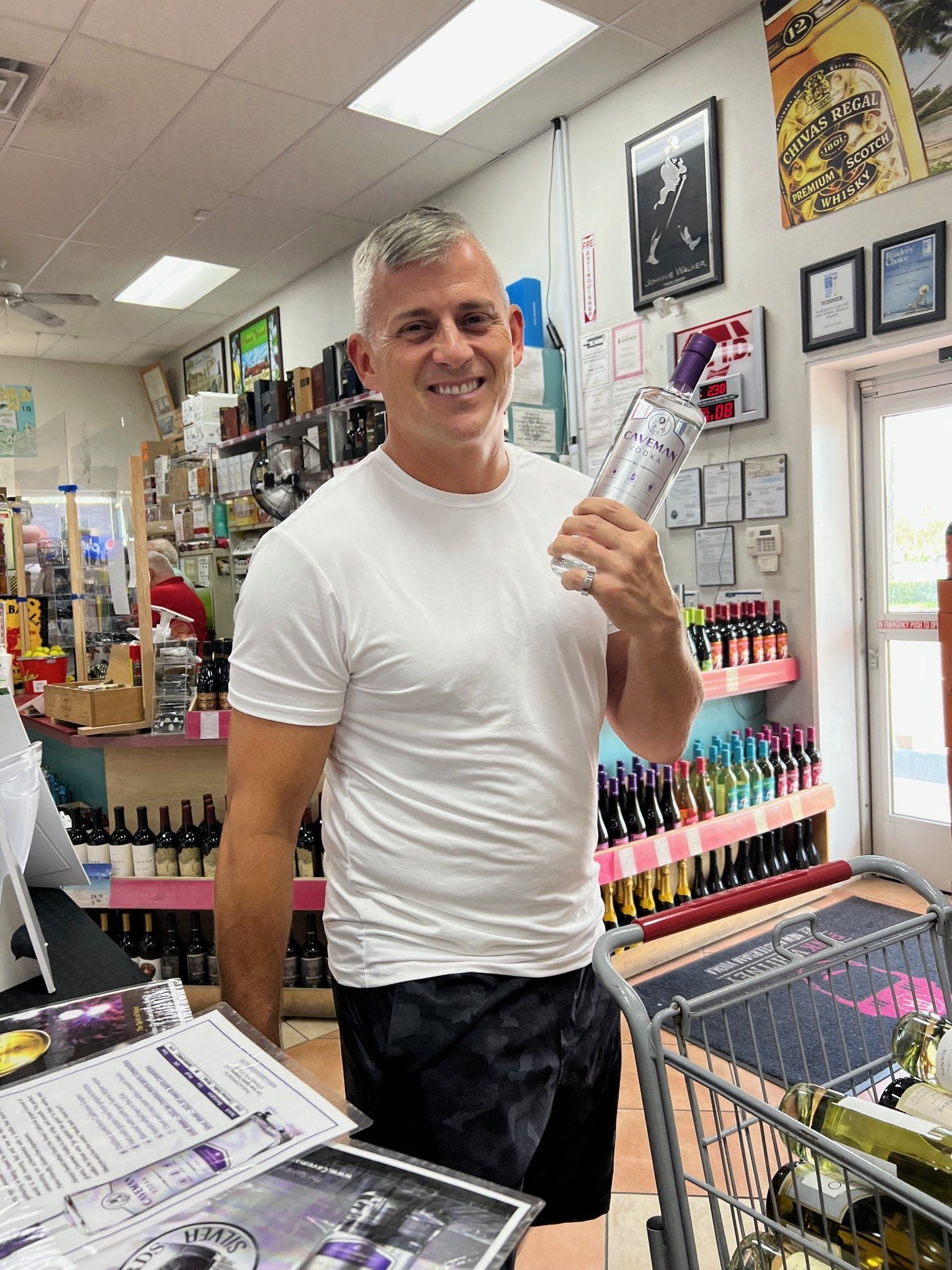 A man in a white shirt is holding a bottle of wine in a store.