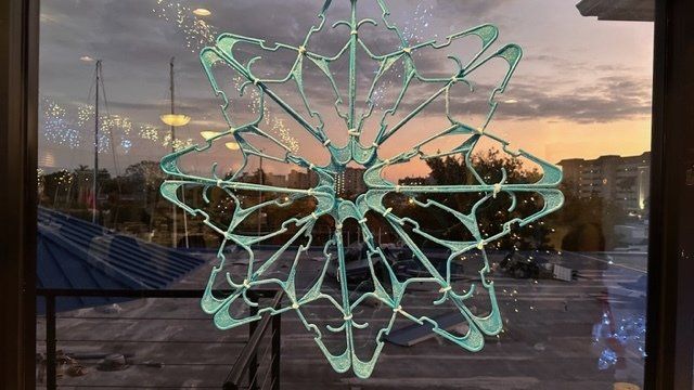 A snowflake made out of clothes hangers is hanging on a window.