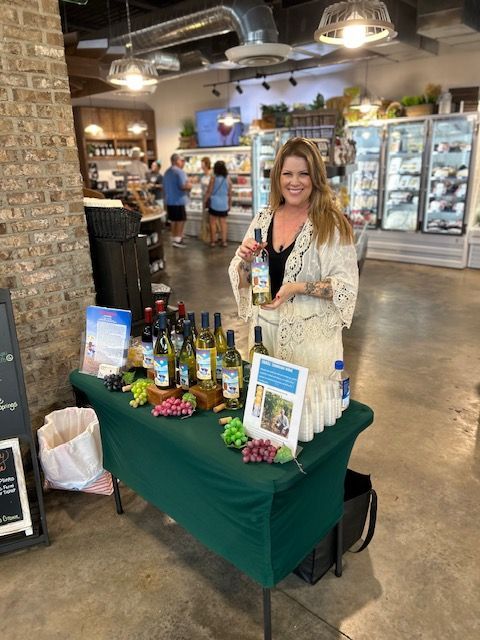 A woman is standing in front of a table holding a bottle of wine.
