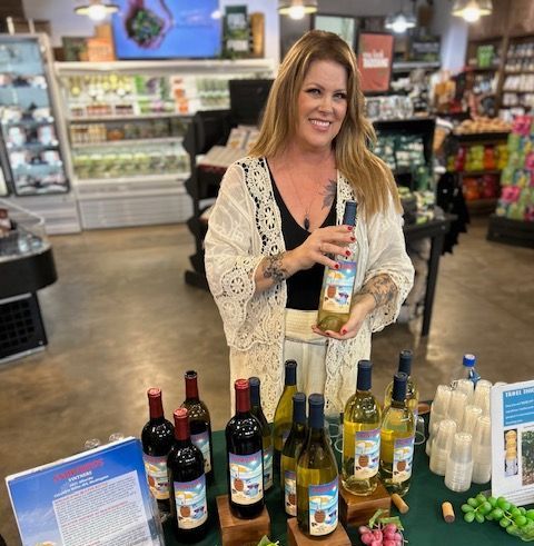 A woman is standing in front of a table full of wine bottles.