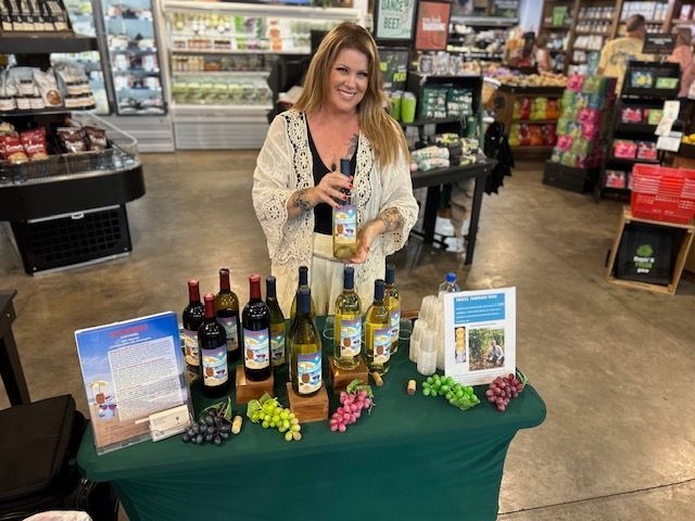 A woman is standing in front of a table with bottles of wine on it.