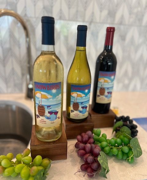 Three bottles of wine are sitting on a counter next to grapes.