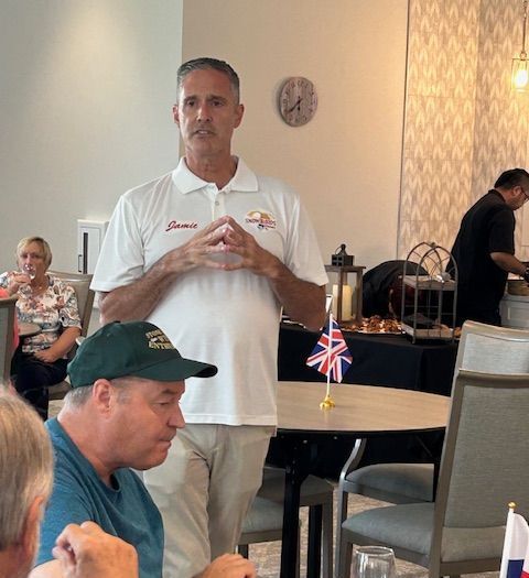 A man in a white shirt stands in front of a table with a british flag on it