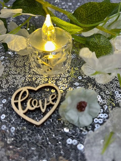 A wooden heart with the word love in it is sitting on a table next to a candle.