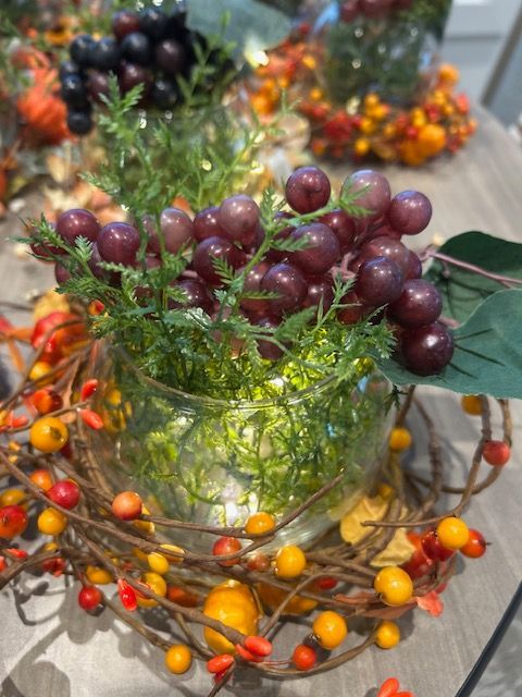 A vase filled with grapes and leaves on a table.