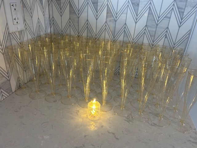 A bunch of champagne flutes are sitting on a counter next to a candle.
